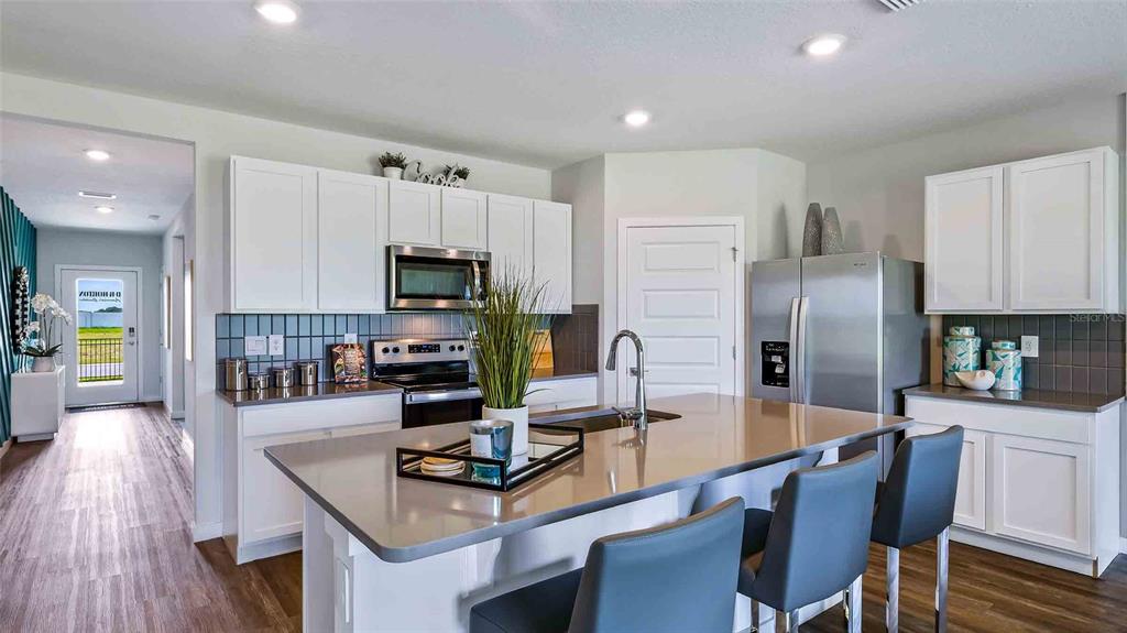 A modern kitchen features white cabinets, a large island with bar seating, and stainless appliances — 18227 BEEHIVE TERRACE, LAKEWOOD RANCH, FL