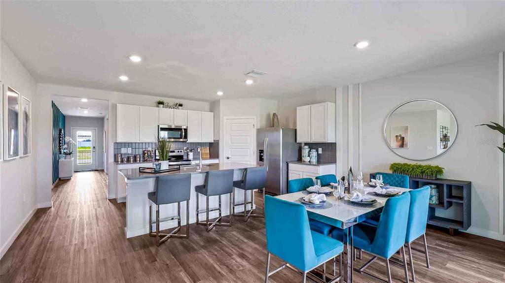 A modern open-concept kitchen and dining area with white cabinetry, blue chairs, and wood flooring — 18227 BEEHIVE TERRACE, LAKEWOOD RANCH, FL