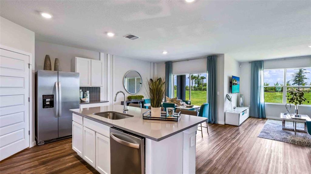 A modern kitchen with a center island and stainless steel appliances opens to a dining area — 18227 BEEHIVE TERRACE, LAKEWOOD RANCH, FL