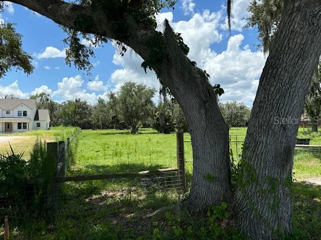 A large oak tree stands in the foreground of a grassy, fenced-in vacant lot — PINE WAY Lot 4E, SANFORD, FL