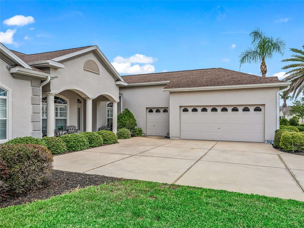 A beige house with a three-car garage and a covered front porch under a blue sky — 12421 SE 174TH LOOP, SUMMERFIELD, FL