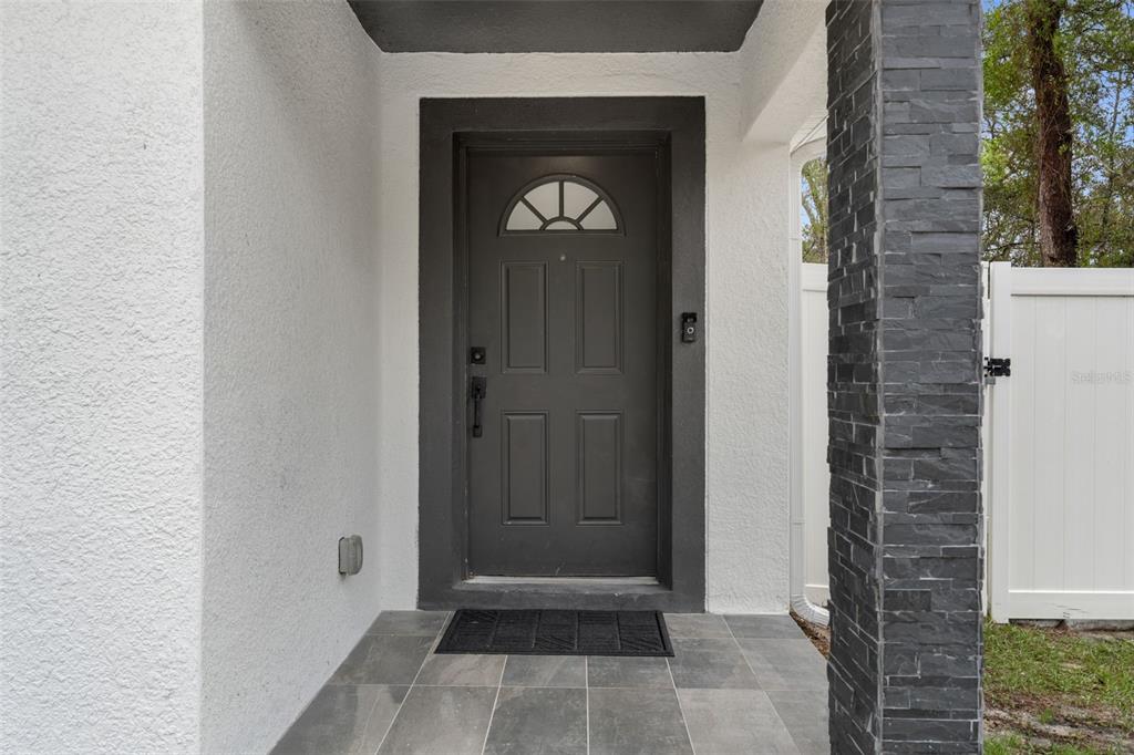 A dark gray front door with a semi-circular window sits under a covered entryway — 5106 PACIFIC AVENUE, SPRING HILL, FL