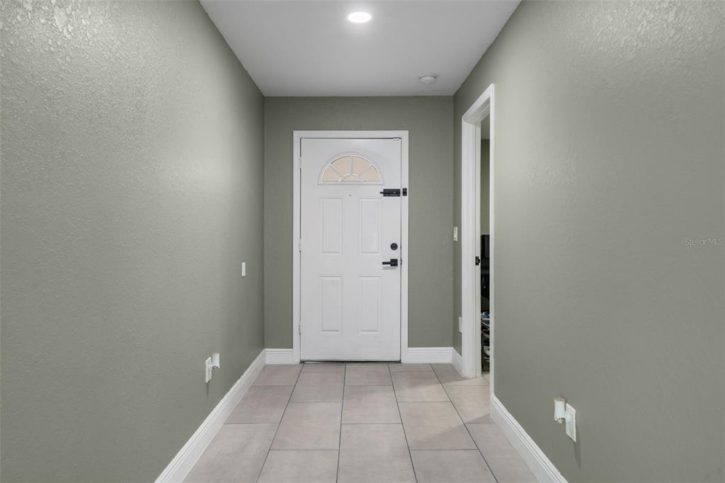 A tiled entryway features sage green walls, a white front door, and a doorway — 5106 PACIFIC AVENUE, SPRING HILL, FL