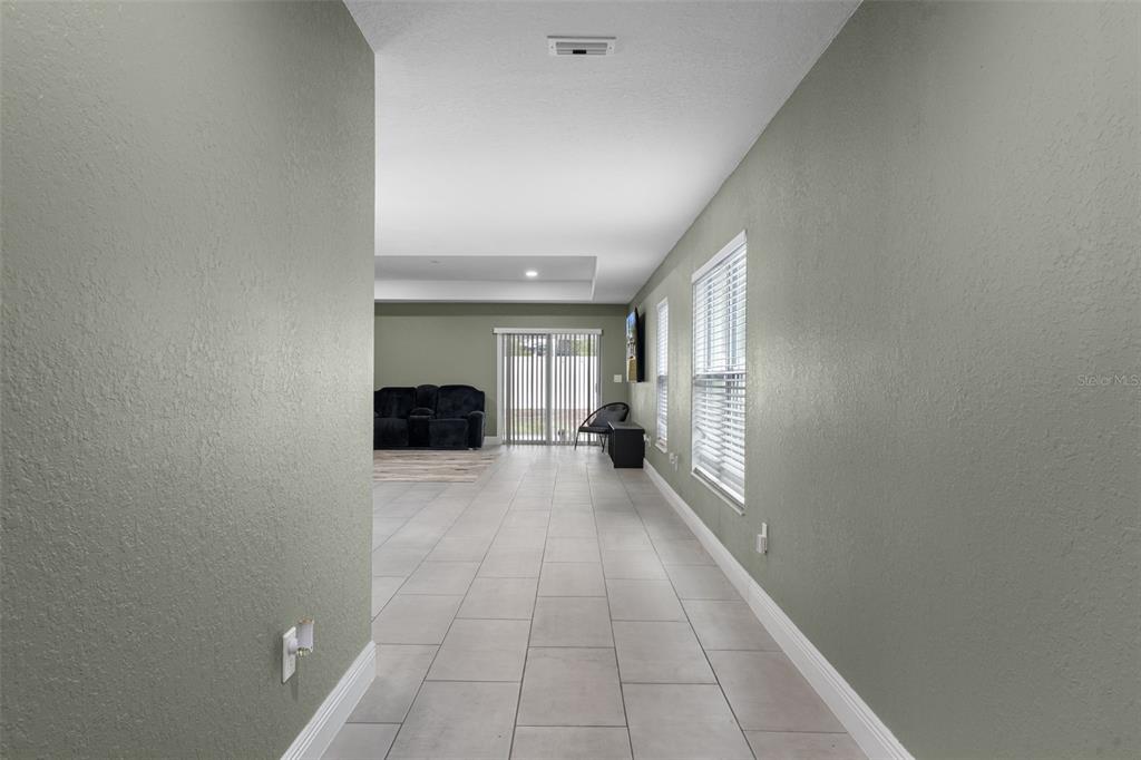 A hallway with light tile flooring leads into a living area with sliding glass doors — 5106 PACIFIC AVENUE, SPRING HILL, FL