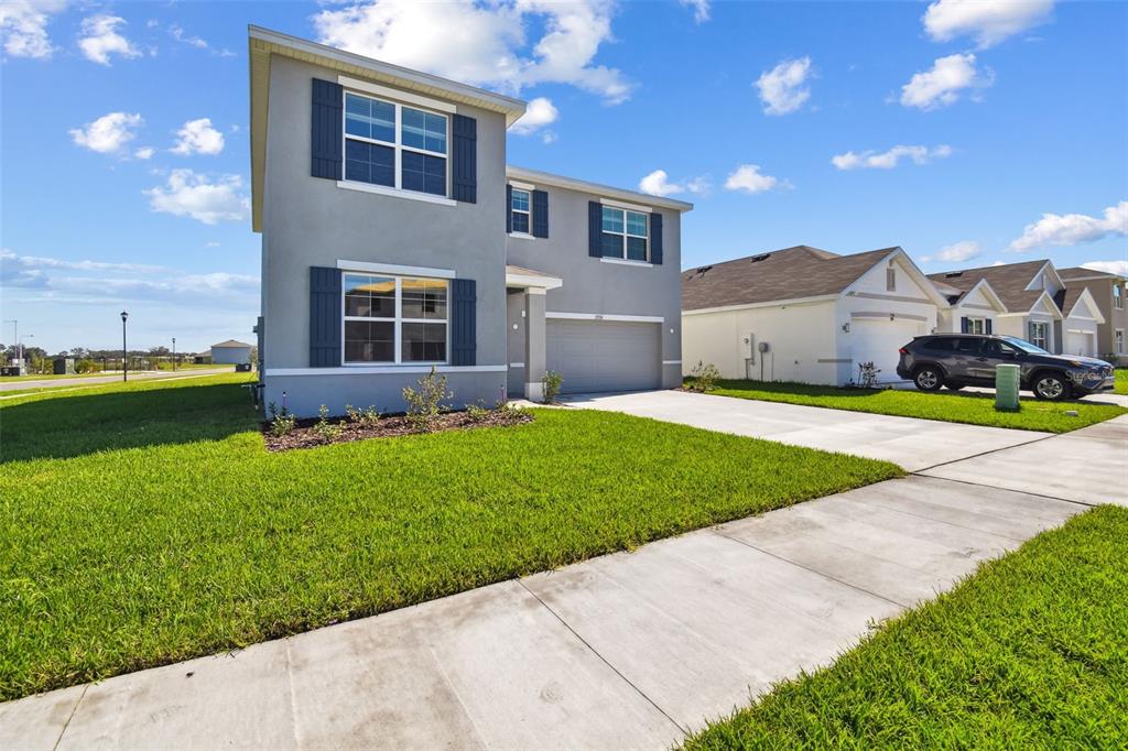 A two-story suburban house with a gray stucco exterior, dark shutters, and a concrete driveway — 2774 COMMON FIG RUN, WESLEY CHAPEL, FL