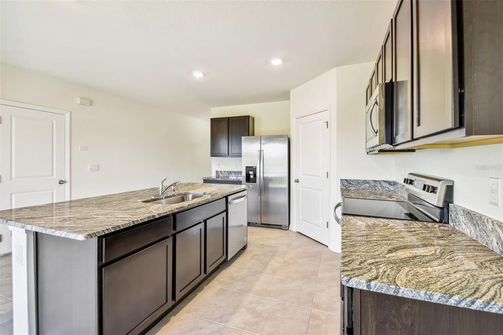 A kitchen features dark wood cabinets, granite countertops, stainless steel appliances, and a central island — 2774 COMMON FIG RUN, WESLEY CHAPEL, FL