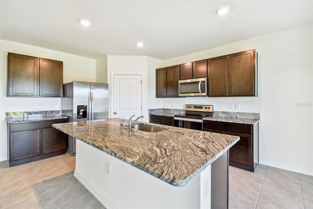 A kitchen features dark wood cabinets, granite countertops, a center island, and stainless steel appliances — 2774 COMMON FIG RUN, WESLEY CHAPEL, FL