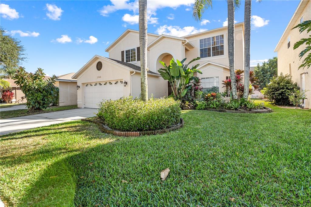 A two-story suburban house features a beige stucco exterior, a garage, and landscaped front yard — 27416 BREAKERS DRIVE, WESLEY CHAPEL, FL