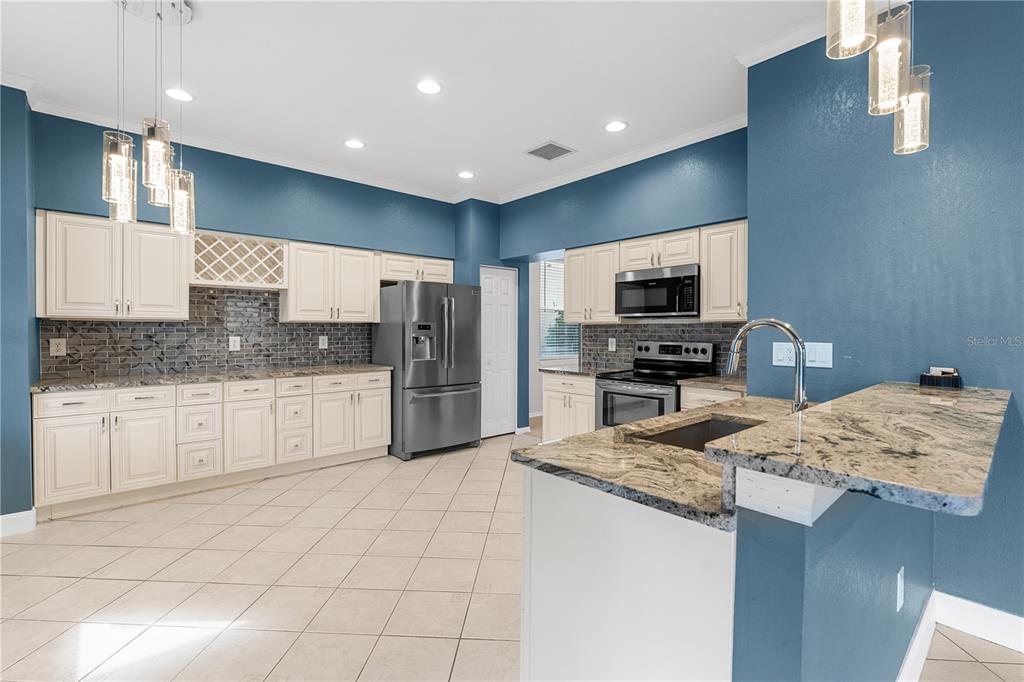 A kitchen features cream cabinets, granite countertops, stainless steel appliances, and blue painted walls — 27416 BREAKERS DRIVE, WESLEY CHAPEL, FL
