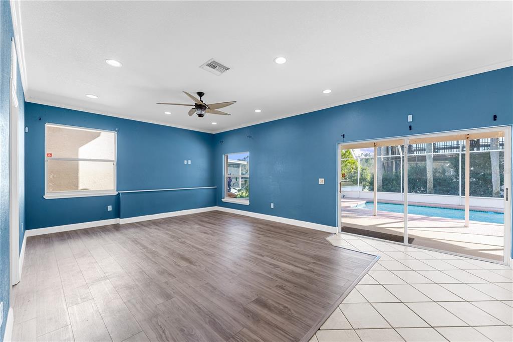A living room with blue walls, wood-look flooring, recessed lighting, and sliding doors to a pool — 27416 BREAKERS DRIVE, WESLEY CHAPEL, FL