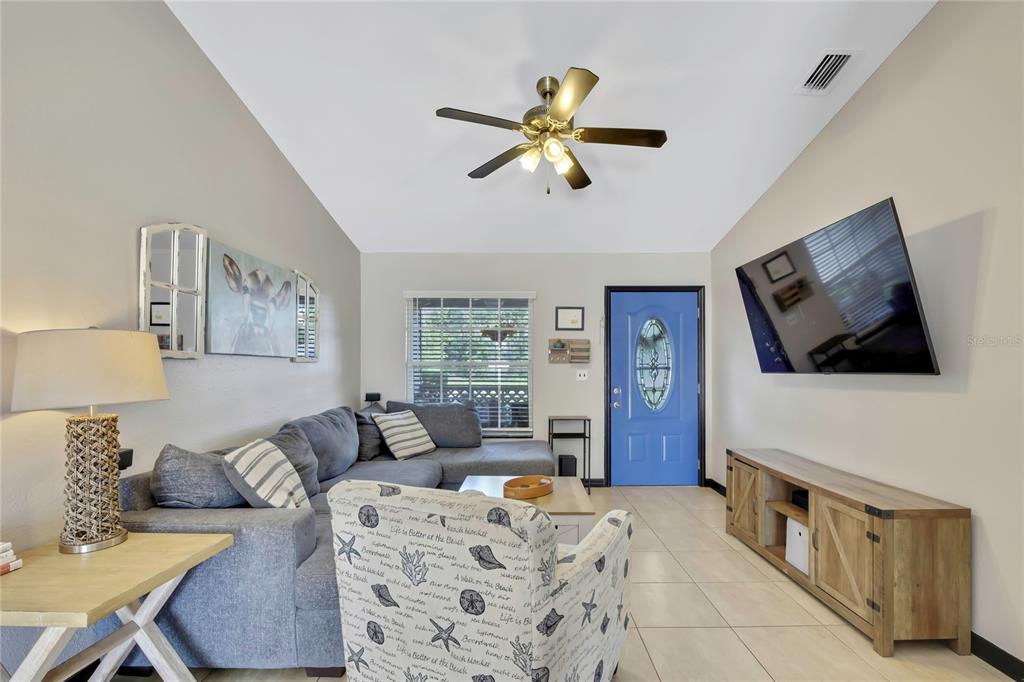 A living room features a gray sectional sofa, a patterned armchair, and a blue front door — 7484 SUSQUEHANNA TRAIL, SPRING HILL, FL