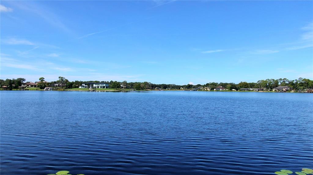 A wide view of a calm lake surrounded by houses and trees under a blue sky — LAKE MARKHAM ROAD, SANFORD, FL