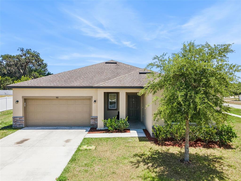 A single-story house with a beige stucco exterior, a two-car garage, and a front tree — 903 SHIMMERING OAKS LANE, SEFFNER, FL
