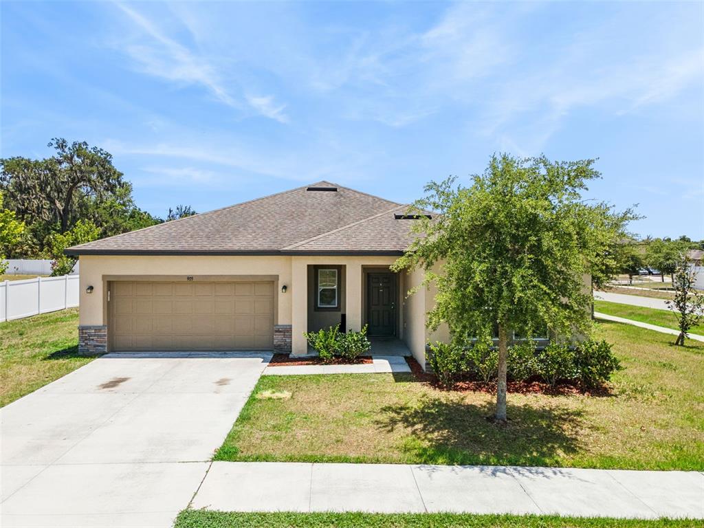 A single-story house with a tan stucco exterior, a two-car garage, and a front lawn — 903 SHIMMERING OAKS LANE, SEFFNER, FL