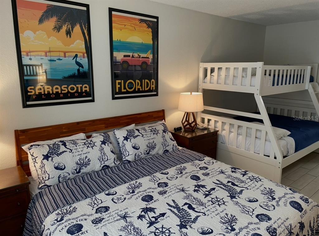 A bedroom features a queen bed with nautical bedding, a white bunk bed, and wall art — 7150 N TAMIAMI TRAIL UNIT N420, SARASOTA, FL