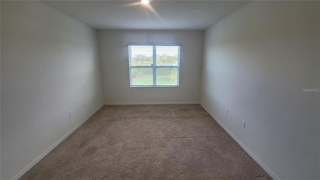 An empty bedroom with beige carpet, white walls, and a window overlooking a fenced yard — 1128 FOX PATH ROAD, DAVENPORT, FL