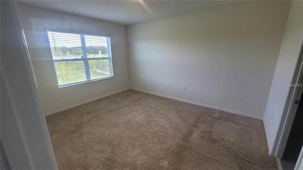 An empty bedroom features beige carpet, light-colored walls, and a window overlooking a grassy yard — 1128 FOX PATH ROAD, DAVENPORT, FL