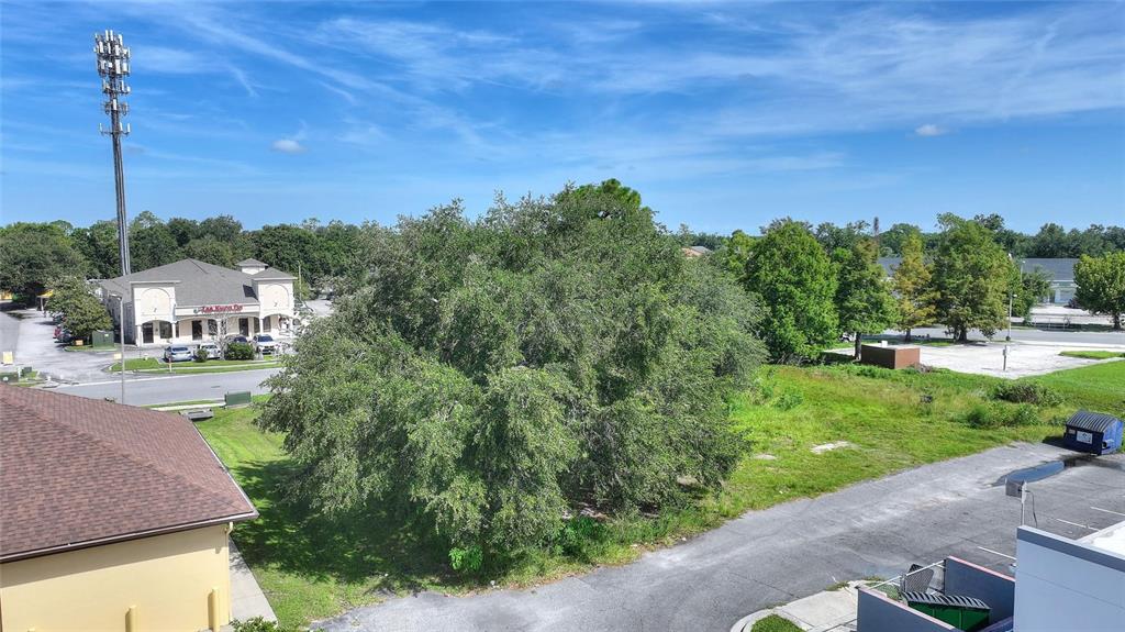An elevated view shows a large tree in a grassy lot near commercial buildings — 0 PLAZA DRIVE NW, KISSIMMEE, FL