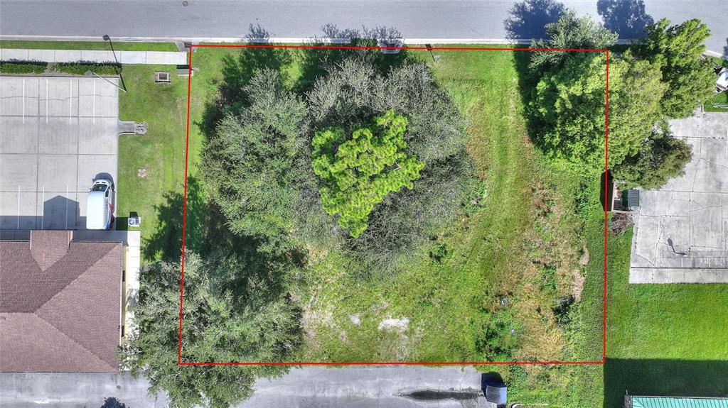 An aerial view shows a rectangular, tree-covered vacant lot outlined in red between two buildings — 0 PLAZA DRIVE NW, KISSIMMEE, FL