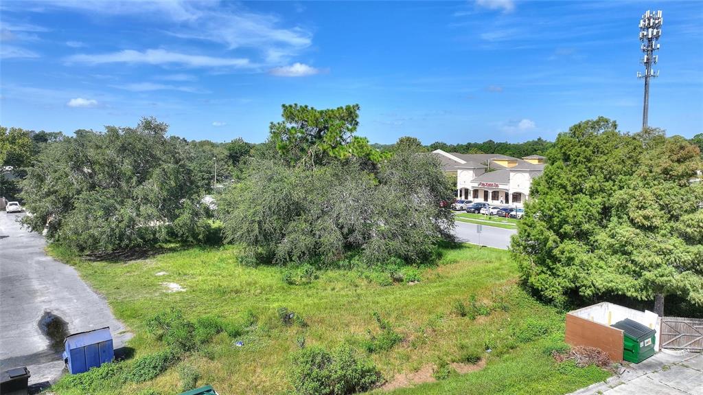 An elevated view of a grassy lot with trees, a dumpster, and a nearby building — 0 PLAZA DRIVE NW, KISSIMMEE, FL