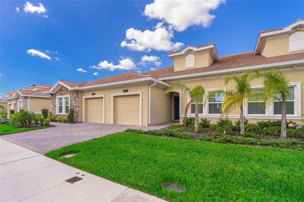 Exterior view of a tan suburban townhome with a two-car garage and palm trees — 1173 TRAPPERS TRAIL LOOP, CHAMPIONS GATE, FL