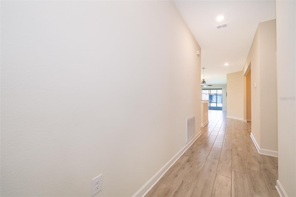 A hallway with light-colored walls and wood-look tile flooring leads toward an open living area — 1173 TRAPPERS TRAIL LOOP, CHAMPIONS GATE, FL