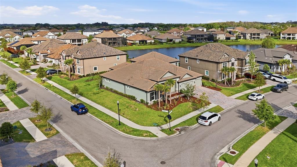 An aerial view shows a suburban neighborhood with houses, a lake, and paved streets — 7073 GRAYBROOK DRIVE, WESLEY CHAPEL, FL
