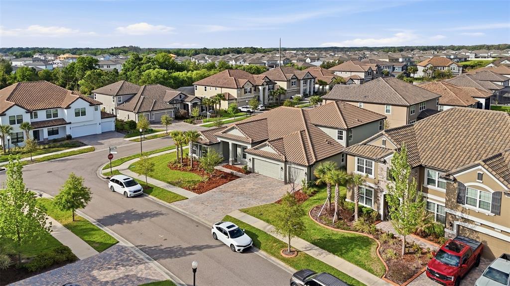 An aerial view shows a suburban neighborhood with multiple houses, paved streets, and parked cars — 7073 GRAYBROOK DRIVE, WESLEY CHAPEL, FL