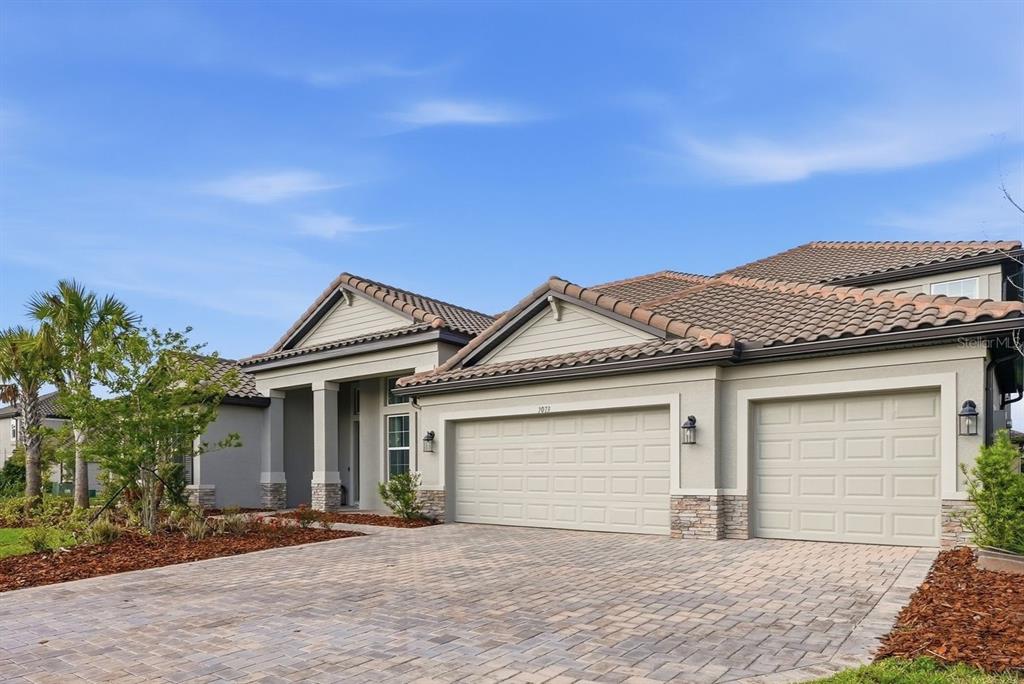 A single-story house with a tile roof, stone accents, and a three-car garage — 7073 GRAYBROOK DRIVE, WESLEY CHAPEL, FL