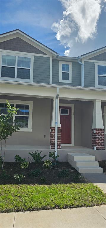 A two-story townhouse exterior with a red front door, covered porch, and brick-accented columns — 180 RAINWOOD STREET, GROVELAND, FL