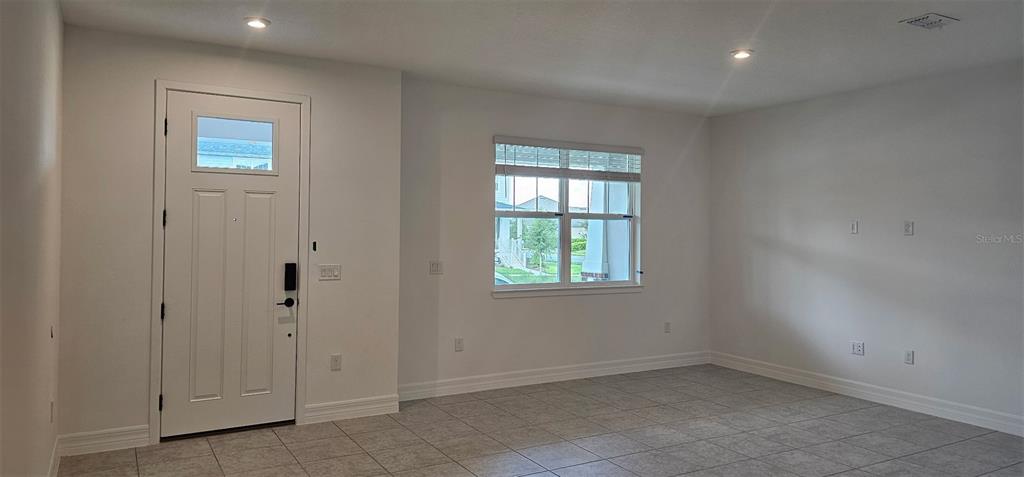 An interior view of a room with white walls, tile flooring, a front door, and window — 180 RAINWOOD STREET, GROVELAND, FL
