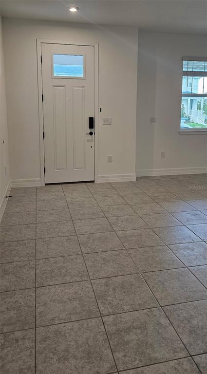 An interior view of a room with light-colored tile flooring, white walls, and a front door — 180 RAINWOOD STREET, GROVELAND, FL