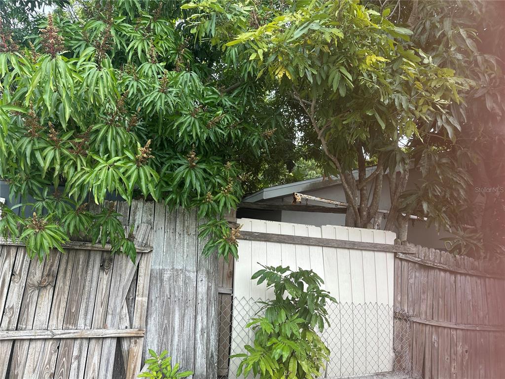 A wooden fence and a chain-link fence stand in front of trees and a building — 12588 128TH AVENUE, LARGO, FL