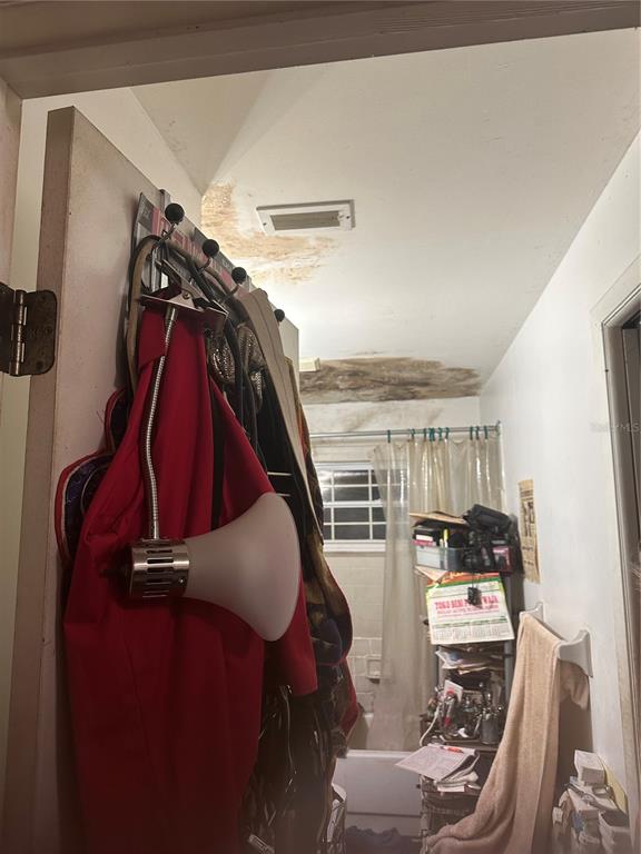 A bathroom with a shower, a door with hanging items, and significant water damage on ceiling — 12588 128TH AVENUE, LARGO, FL