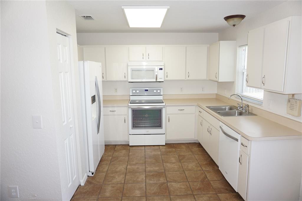 A kitchen features white cabinetry, white appliances, tan countertops, and brown tile flooring — 6655 NW 15TH AVENUE, OCALA, FL
