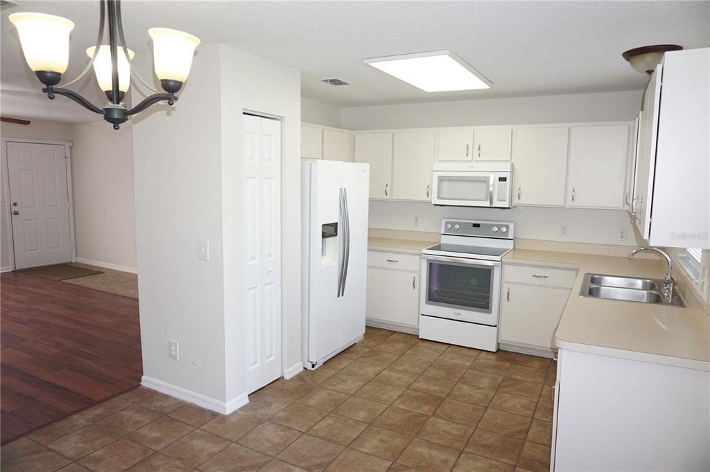 A kitchen features white cabinets, white appliances, tan countertops, and brown tile flooring — 6655 NW 15TH AVENUE, OCALA, FL