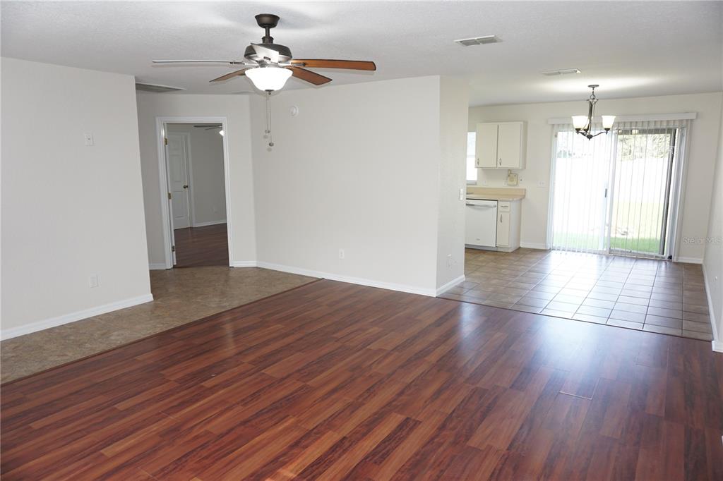 An open living area with wood-look flooring, a ceiling fan, and an adjacent tiled kitchen — 6655 NW 15TH AVENUE, OCALA, FL