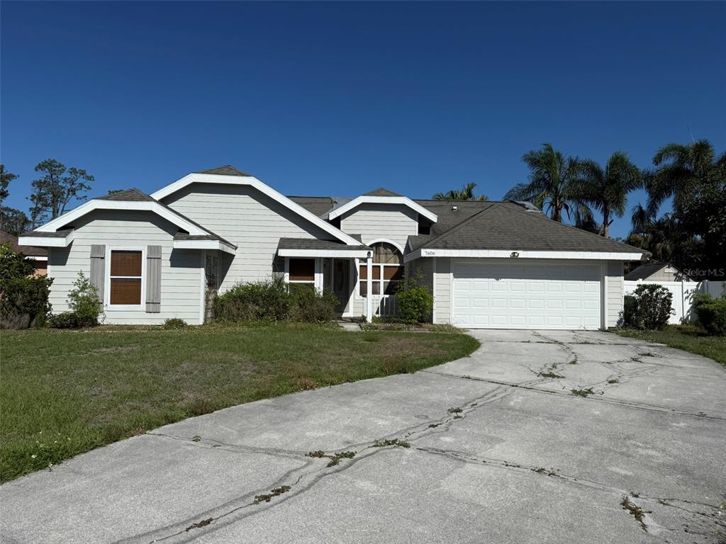 A single-story house with light gray siding, a white garage door, and a cracked concrete driveway — 7606 37TH STREET CIRCLE E, SARASOTA, FL