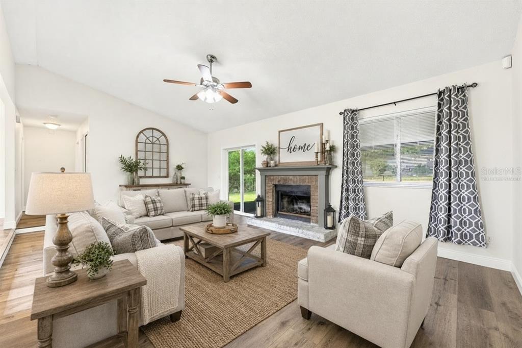 A living room with a fireplace, beige furniture, a wooden coffee table, and hardwood floors — 745 MENTMORE CIRCLE, DELTONA, FL