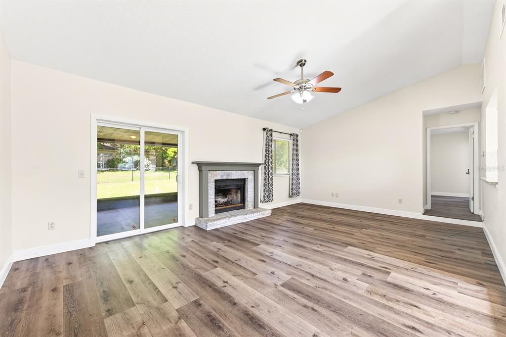 A living room features wood-look flooring, a brick fireplace, a ceiling fan, and sliding doors — 745 MENTMORE CIRCLE, DELTONA, FL
