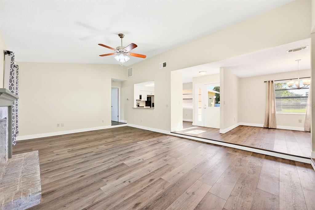 A spacious living room features wood-look flooring, a vaulted ceiling with a fan, and a fireplace — 745 MENTMORE CIRCLE, DELTONA, FL