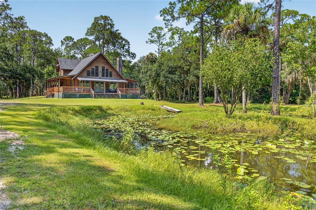 A wooden cabin with a wrap-around porch sits beside a pond with lily pads — 5365 PACES LANDING ROAD, MIMS, FL