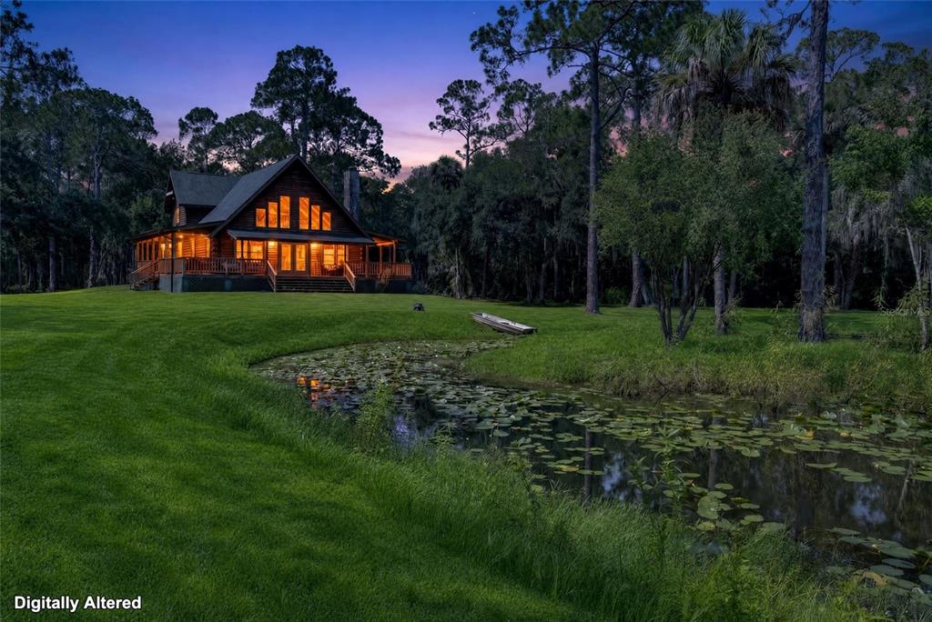 A two-story log cabin sits beside a small pond in a grassy, wooded landscape — 5365 PACES LANDING ROAD, MIMS, FL