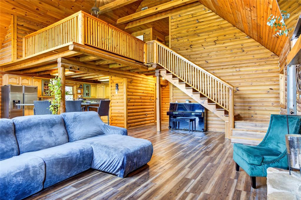 A living room with a blue sectional, teal armchair, piano, and wooden walls and stairs — 5365 PACES LANDING ROAD, MIMS, FL