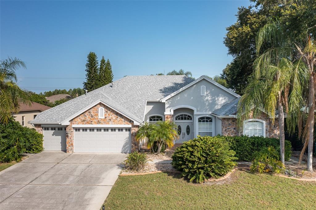 A single-story house with a stone facade, a two-car garage, and a palm tree-lined lawn — 2151 EDELWEISS LOOP, TRINITY, FL