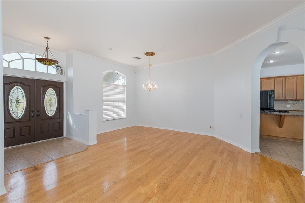 An empty dining room with hardwood floors, a crystal chandelier, and an arched kitchen doorway — 2151 EDELWEISS LOOP, TRINITY, FL