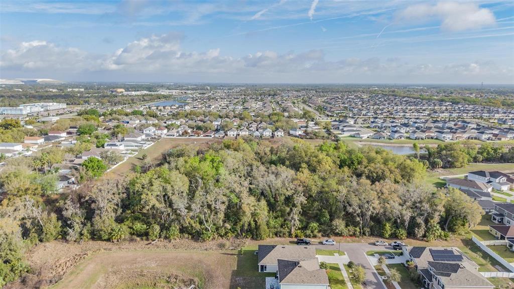 An aerial view shows a wooded lot situated between residential neighborhoods and a small pond — MIRACLE MILE, RIVERVIEW, FL