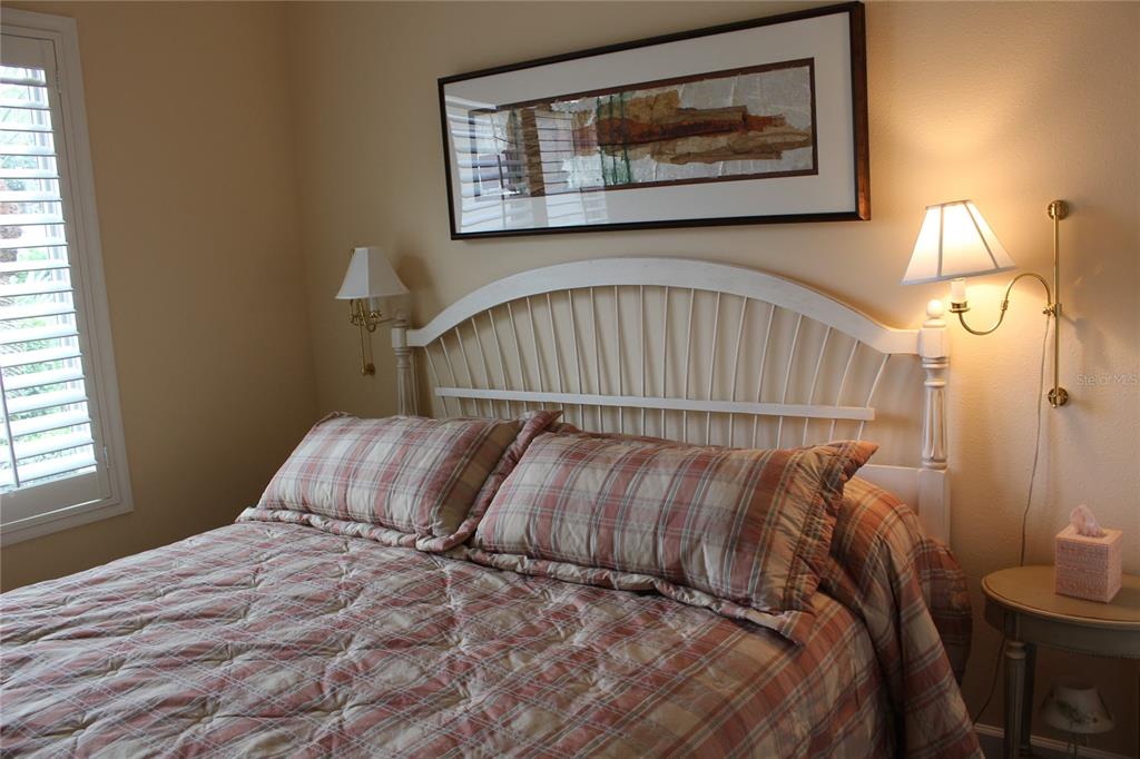 A bedroom features a white spindle headboard, plaid bedding, wall-mounted lamps, and a framed artwork — 5215 97TH STREET E, BRADENTON, FL