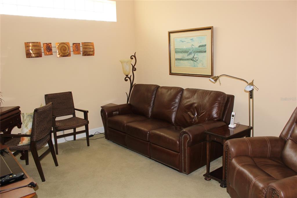 A living room features a brown leather sofa, matching armchair, two chairs, and wall art — 5215 97TH STREET E, BRADENTON, FL