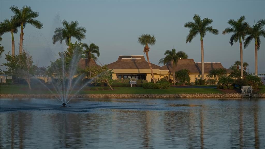 A fountain sprays water in a lake in front of a clubhouse with palm trees — 707 BLANCA, NORTH PORT, FL